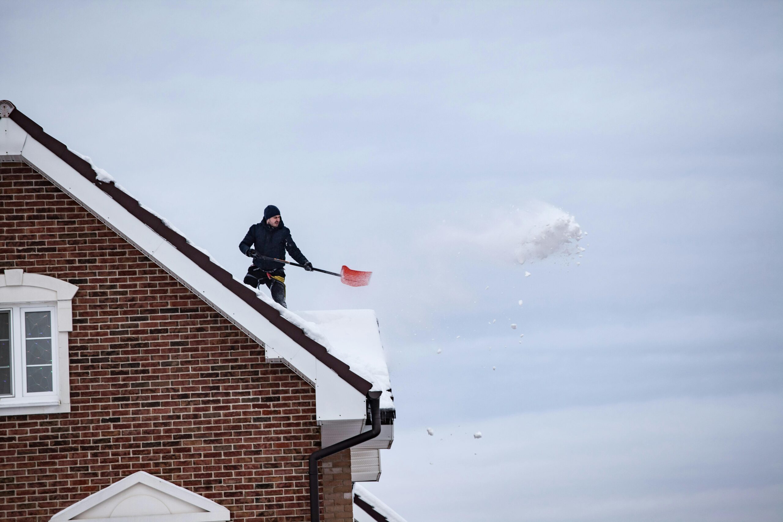A man shoveling snow off a rooftop, indicating winter outdoor activity.